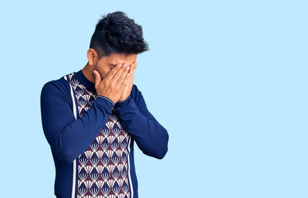 泣きながら手で顔を覆う悲しい表情のカジュアルな冬のセーターを着たハンサムなラテン系アメリカ人の若者。うつ病の概念.  - 写真・画像