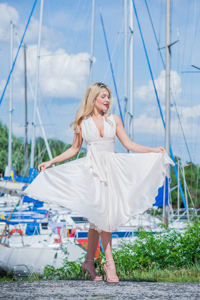 Nice blonde lady in yacht club. Woman in flying silk white dress at outdoor, relax time - Фото, изображение