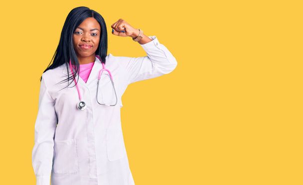 Fiatal afro-amerikai nő visel orvos sztetoszkóp erős személy mutatja kar izom, magabiztos és büszke hatalom  - Fotó, kép