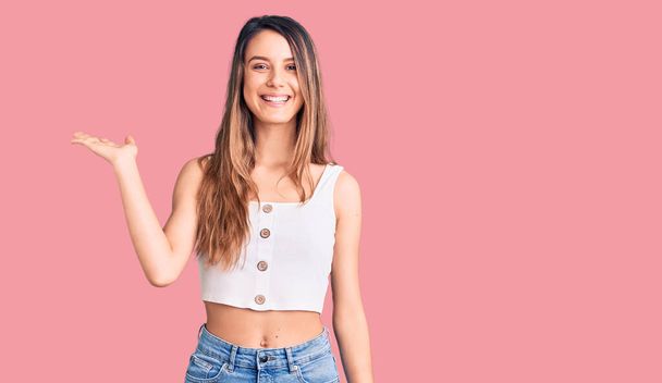 Young beautiful girl wearing casual sleeveless t shirt smiling cheerful presenting and pointing with palm of hand looking at the camera.  - Photo, Image