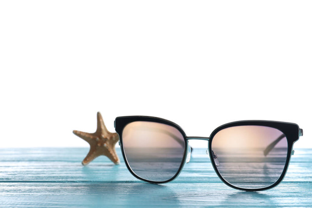 Stylish sunglasses and starfish on light blue wooden table against white background - Φωτογραφία, εικόνα