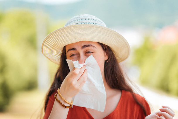 藁帽子の女性はハンカチで彼女の鼻を吹く。屋外。アレルギーとウイルスの概念. - 写真・画像