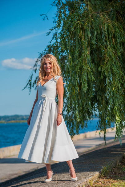 Elegante mujer de pelo rubio en midi vestido blanco en la orilla. Concepto o código blanco, señora de moda, vestido bonito y ropa - Foto, imagen