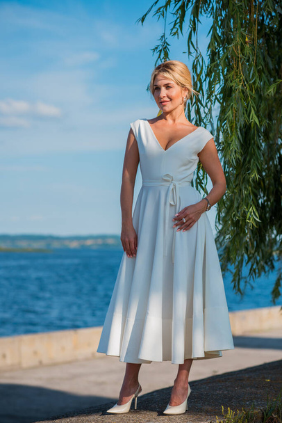 Elegante mujer de pelo rubio en midi vestido blanco en la orilla. Concepto o código blanco, señora de moda, vestido bonito y ropa - Foto, imagen