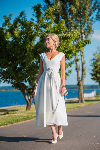 Elegant blonde hair woman in white midi dress at shore. Concept o white code, fashionable lady, pretty dress and clothes - Foto, Bild