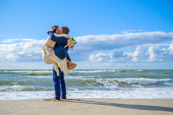 Χαρούμενη νύφη και γαμπρός αγκαλιασμένοι στην παραλία - Φωτογραφία, εικόνα