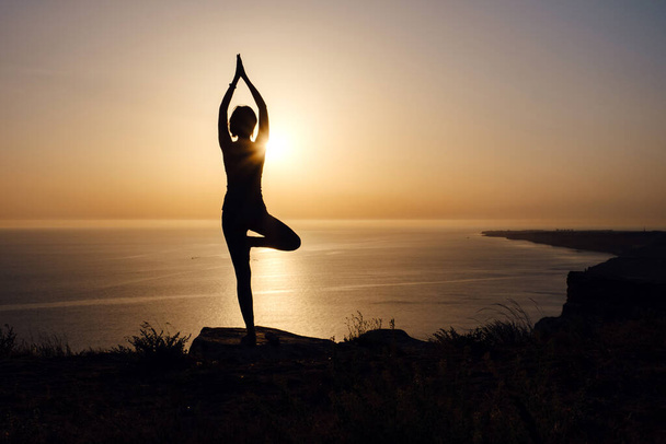 Žena s jógovým postojem na hoře při západu slunce Silueta nádherné mladé ženy cvičit jógu venku. wellness, zdravotní péče, sport a životní styl koncept - Fotografie, Obrázek