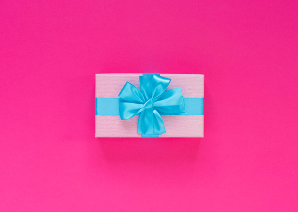 Pink gift box with blue bow and ribbon on  paper background with empty place for text. Copy space for text. Flat lay, top view concept. - 写真・画像