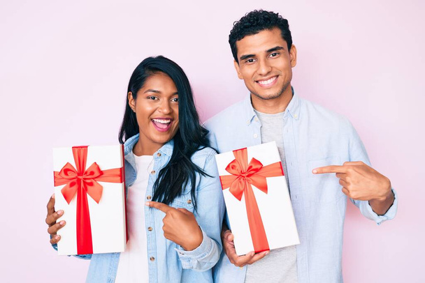 Schönes lateinisches junges Paar mit Geschenk für Jubiläumsfeier lächelnd glücklich mit Hand und Finger zeigend  - Foto, Bild