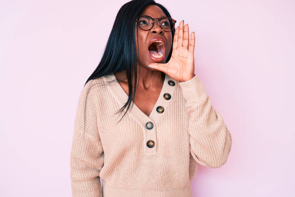 Mujer afroamericana joven con ropa casual gritando y gritando fuerte a un lado con la mano en la boca. concepto de comunicación.  - Foto, imagen