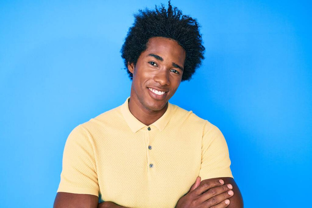 Bonito homem americano africano com cabelo afro vestindo roupas casuais rosto feliz sorrindo com os braços cruzados olhando para a câmera. pessoa positiva.  - Foto, Imagem