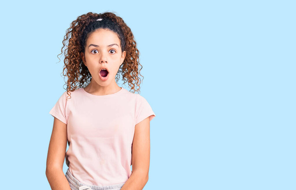 Beautiful kid girl with curly hair wearing casual clothes afraid and shocked with surprise expression, fear and excited face.  - Photo, Image