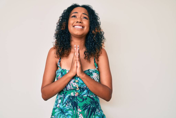 Fiatal afro-amerikai nő alkalmi ruhát visel koldulás és imádkozás kéz a kézben együtt remény kifejezés az arcon nagyon érzelmes és aggódik. Könyörgök..  - Fotó, kép