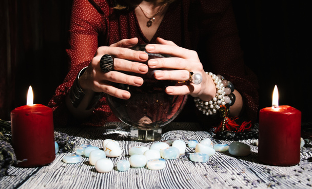 As mãos do Fortuneteller numa esfera de vidro. Previsão do futuro. Interior místico. Símbolos ocultos, pedras runas, rosários, velas - Foto, Imagem
