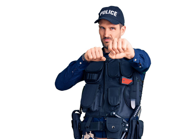 Mladý pohledný muž v policejní uniformě děrování pěst do boje, agresivní a naštvaný útok, hrozba a násilí  - Fotografie, Obrázek