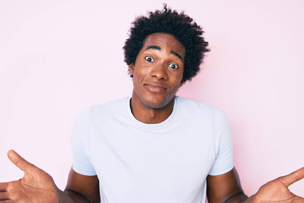 Handsome african american man with afro hair wearing casual clothes clueless and confused expression with arms and hands raised. doubt concept.  - Фото, зображення