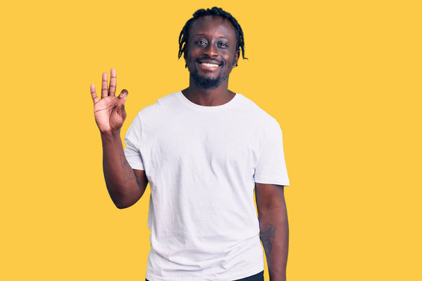 Jonge Afro-Amerikaanse man met vlechten in casual witte tshirt tonen en wijzen met vingers nummer drie, terwijl glimlachen zelfverzekerd en gelukkig.  - Foto, afbeelding