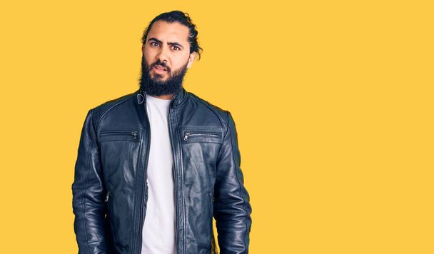 Young arab man wearing casual leather jacket in shock face, looking skeptical and sarcastic, surprised with open mouth  - 写真・画像