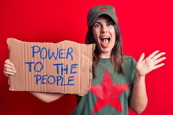 Mooie vrouw draagt t-shirt met rode ster communistisch symbool vragen om sociale beweging vieren prestatie met vrolijke glimlach en winnaar uitdrukking met opgeheven hand - Foto, afbeelding