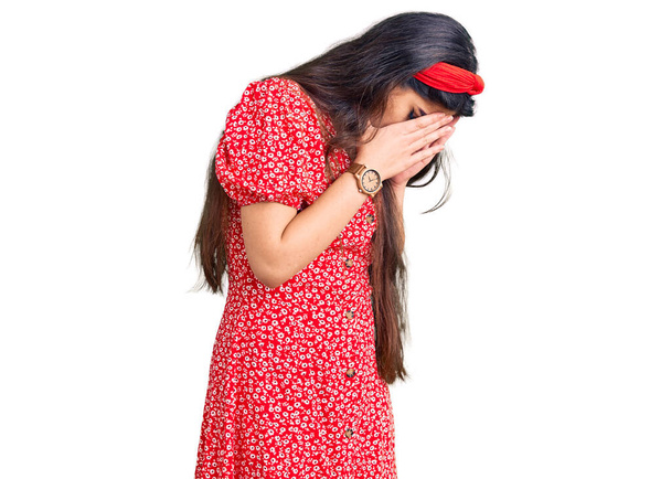 Brünettes Teenager-Mädchen im Sommerkleid mit traurigem Gesichtsausdruck, das Gesicht mit Händen bedeckt, während es weint. Depressionskonzept.  - Foto, Bild
