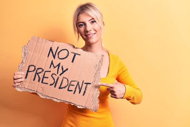 Young blonde woman asking for democracy holding banner with not my president message smiling happy pointing with hand and finger - Foto, Imagen