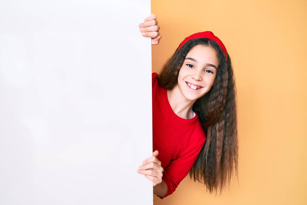 Aranyos spanyol gyerek lány kezében üres banner néz pozitív és boldog álló és mosolygó magabiztos mosollyal mutatja fogak  - Fotó, kép