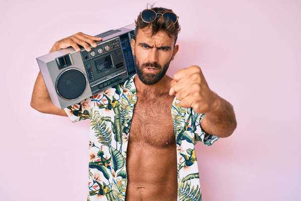Giovane uomo ispanico indossa vestiti estivi che tengono boombox, ascoltando la musica sorridente allegro punta con mano e dito verso il basso  - Foto, immagini
