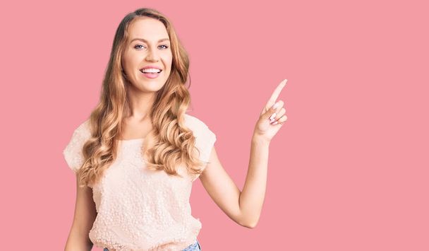 Young beautiful caucasian woman with blond hair wearing casual clothes with a big smile on face, pointing with hand finger to the side looking at the camera.  - Photo, image