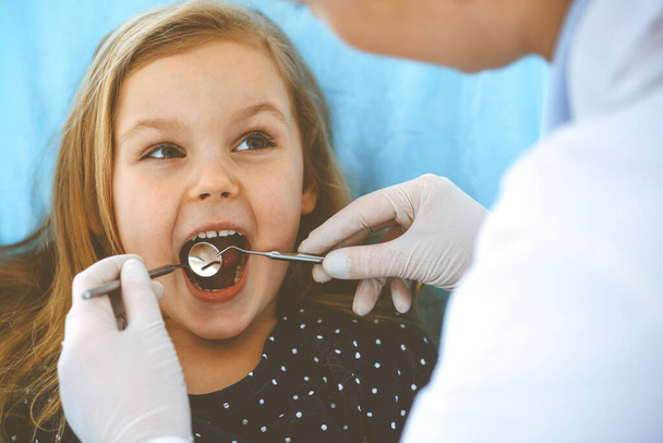 Menina sentada na cadeira dentária com a boca aberta durante o check-up oral, enquanto médico. Consulta ao dentista. Conceito de medicina. Foto tonificada
 - Foto, Imagem