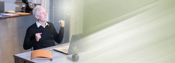 Smiling senior businessman showing success gesture in front of his laptop; panoramic banner - Fotoğraf, Görsel