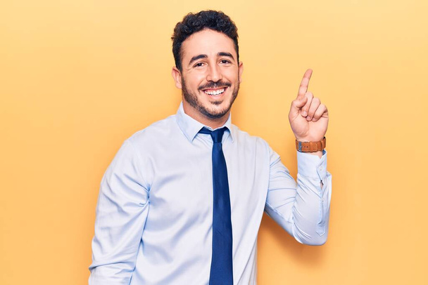 Jonge Latijns-Amerikaanse man in zakelijke kleding glimlachend met een idee of vraag wijzend met een vrolijk gezicht, nummer één  - Foto, afbeelding