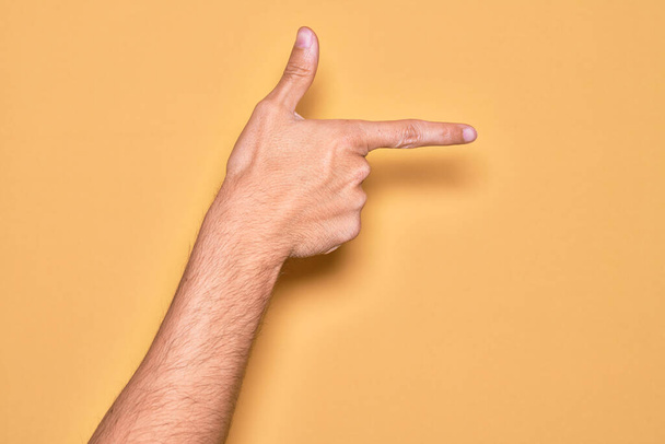 Valkoihoisen nuorukaisen käsi osoittaa sormella eristettyä keltaista taustaa ja osoittaa etusormella sivulle. - Valokuva, kuva