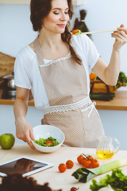 Молодая брюнетка готовит на кухне. Домохозяйка держит в руке деревянную ложку. Концепция питания и здоровья - Фото, изображение