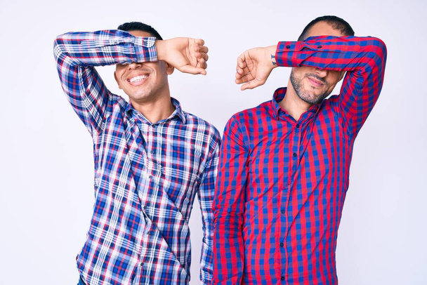 Młoda gejowska para dwóch mężczyzn w luźnych ciuchach przykrywających oczy wesołym i zabawnym ramieniem. ślepa koncepcja.  - Zdjęcie, obraz
