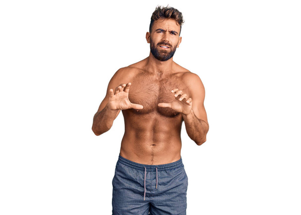 Young hispanic man wearing swimwear shirtless disgusted expression, displeased and fearful doing disgust face because aversion reaction. with hands raised  - Photo, Image