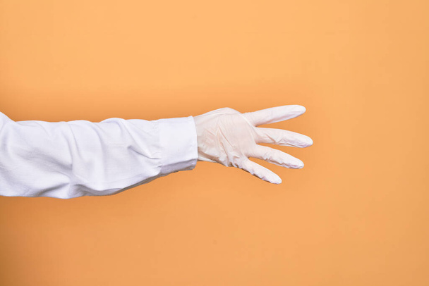 Hand of a person wearing medical surgical glove doing number four with fingers over isolated yellow background - Fotoğraf, Görsel