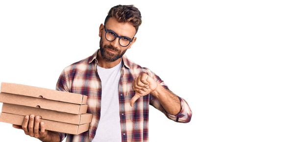 Jovem hispânico segurando caixa de pizza entrega com rosto irritado, sinal negativo mostrando desgosto com os polegares para baixo, conceito de rejeição  - Foto, Imagem