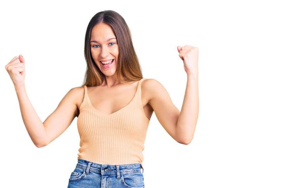 Beautiful brunette young woman wearing casual clothes screaming proud, celebrating victory and success very excited with raised arms  - Foto, Imagen