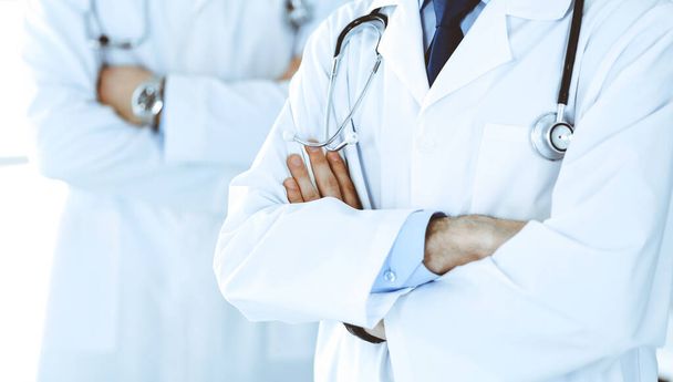 Doctor man standing straight and crossed arms with colleague at background, close-up. Group of doctors. Perfect medical service in clinic. Medicine and healthcare concepts. Toned picture - Φωτογραφία, εικόνα