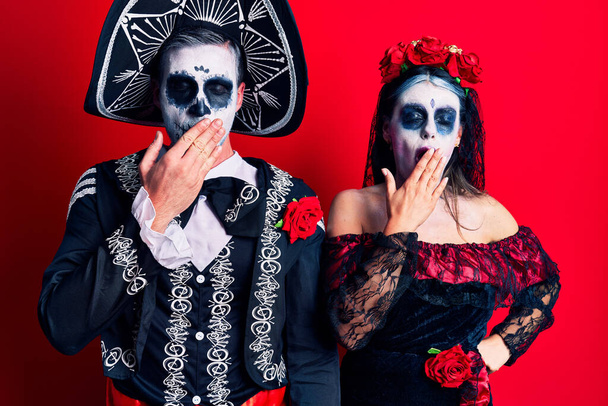 Young couple wearing mexican day of the dead costume over red bored yawning tired covering mouth with hand. restless and sleepiness.  - Photo, Image