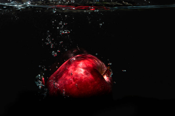 Manzana cayendo en agua aislada sobre fondo negro. - Foto, imagen