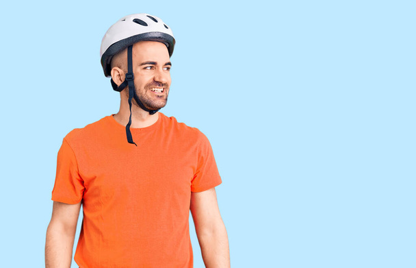 Молодой красивый мужчина в велосипедном шлеме смотрит в сторону с улыбкой на лице, естественным выражением лица. смеясь уверенно.  - Фото, изображение