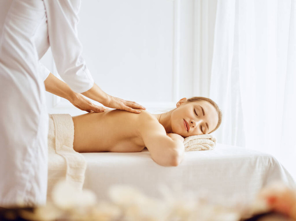 Beautiful woman enjoying back massage with closed eyes - 写真・画像