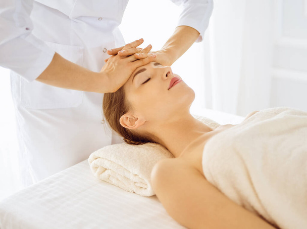 Beautiful woman enjoying facial massage with closed eyes in spa center. Relaxing treatment concept in medicine - Fotó, kép