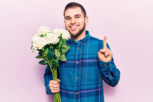 Elinde bir buket çiçekle gülümseyen genç yakışıklı bir adam bir fikir veya soru işareti ile mutlu bir yüzle, bir numara  - Fotoğraf, Görsel