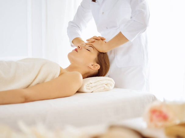 Beautiful woman enjoying facial massage with closed eyes in spa center. Relaxing treatment concept in medicine - Foto, Imagem