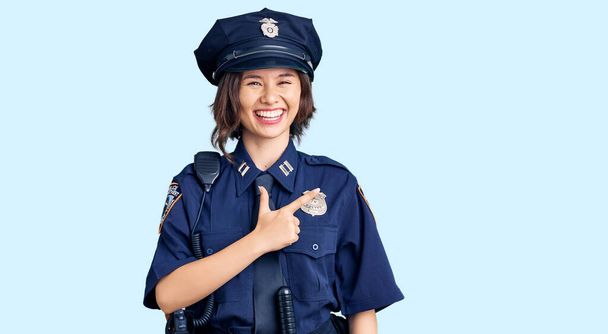 Mladá krásná dívka v policejní uniformě veselý s úsměvem obličeje ukazuje rukou a prstem nahoru na stranu se šťastným a přirozeným výrazem na tváři  - Fotografie, Obrázek