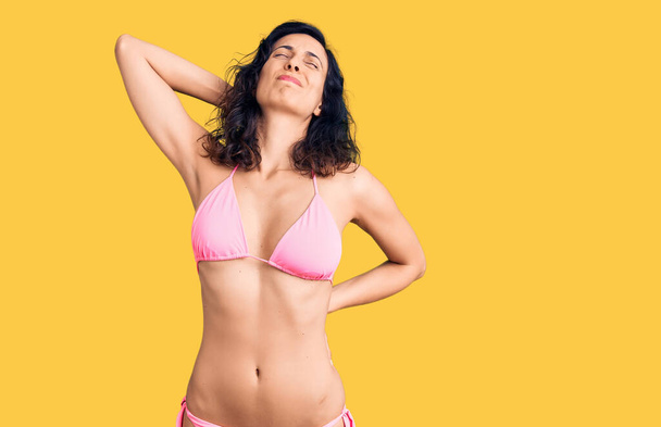 Fiatal gyönyörű spanyol nő visel bikini szenved nyakfájás sérülés, megható nyak kézzel, izomfájdalom  - Fotó, kép