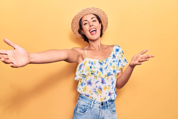 Young beautiful woman wearing summer hat looking at the camera smiling with open arms for hug. cheerful expression embracing happiness.  - Photo, Image