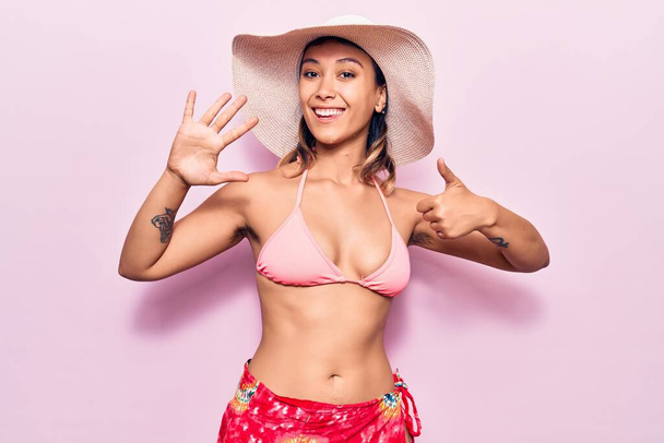 Young woman wearing bikini and hat showing and pointing up with fingers number six while smiling confident and happy.  - Foto, Imagem